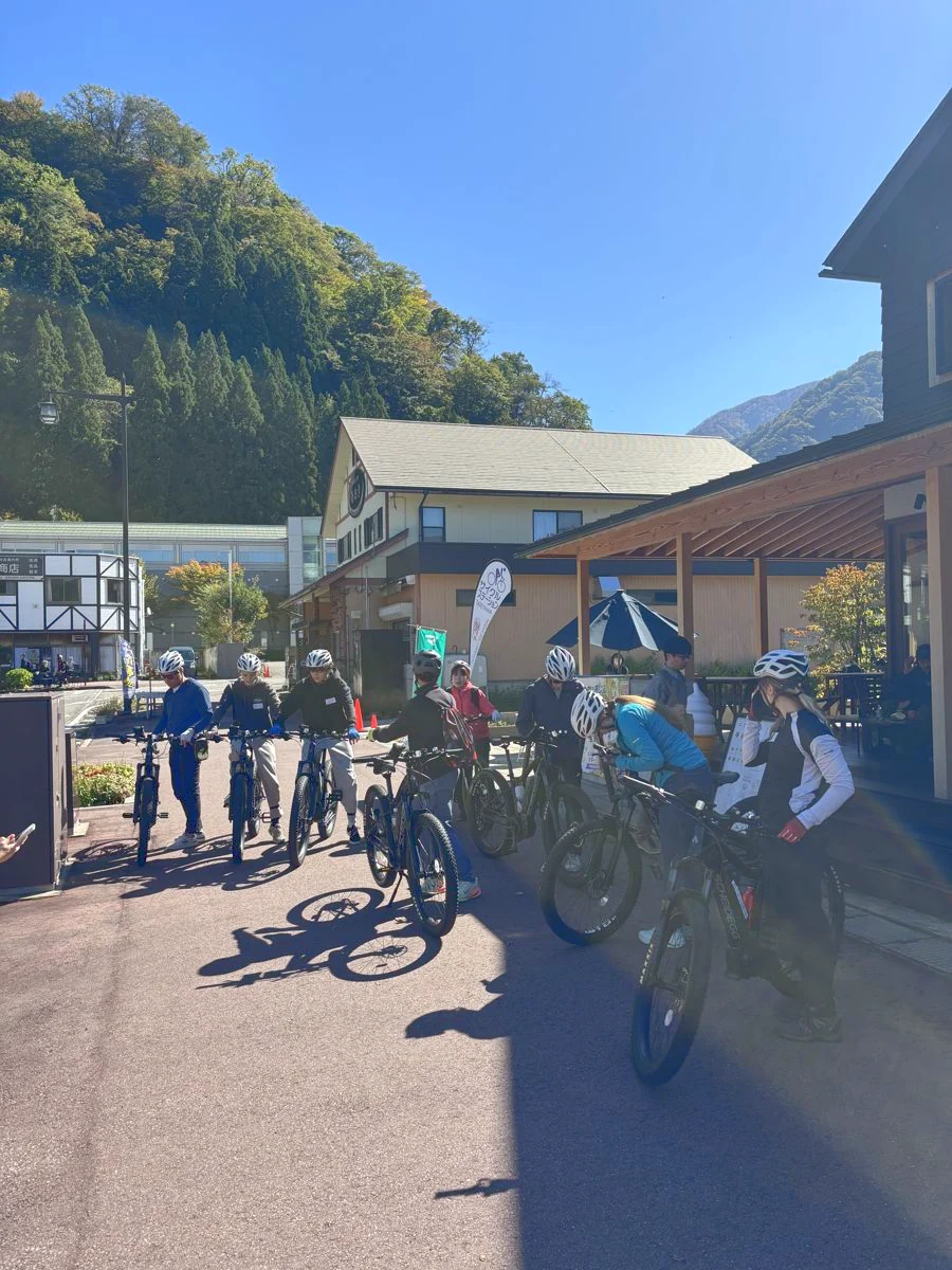 観光案内所の前にE-BIKEを並べ、出発を待つ参加者。背後に山が見える