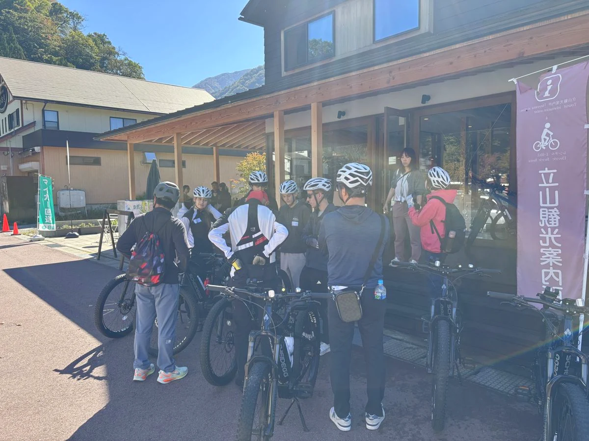 立山駅前の観光案内所の前で、ヘルメットをかぶりE-BIKEの準備をする参加者